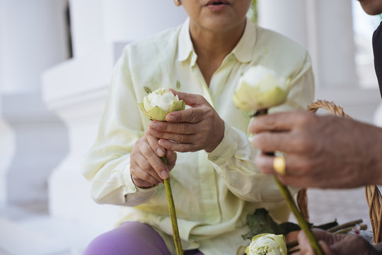 亚洲老年夫妇手持莲花在寺庙里做功德。