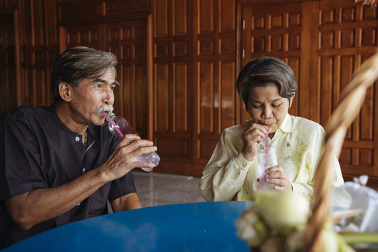 亚洲老年人在亭子庙里用稻草从瓶子里喝水。