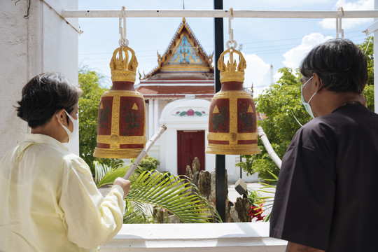 亚洲老年夫妇戴着面具在庙里敲钟许愿。