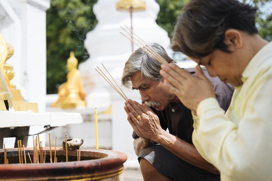 亚洲老年夫妇手持香火在泰国寺庙里敬拜。