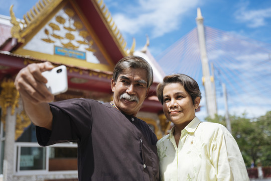 亚洲老年夫妇在泰国寺庙用智能手机自拍。