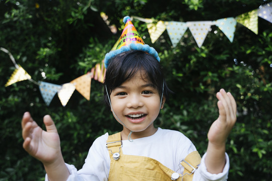 快乐的亚洲黑发孩子的画像戴派对帽在院子里庆祝生日。