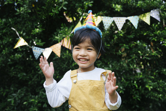 快乐的亚洲黑发孩子的画像戴派对帽在院子里庆祝生日。