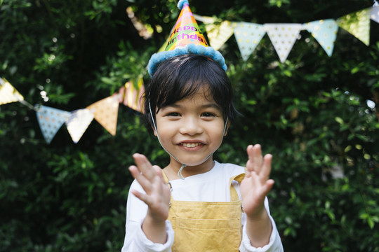 快乐的亚洲黑发孩子的画像戴派对帽在院子里庆祝生日。