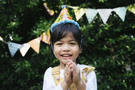 快乐的亚洲黑发孩子的画像戴派对帽在院子里庆祝生日。