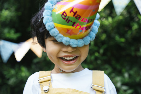 快乐的亚洲黑发孩子的画像戴派对帽在院子里庆祝生日。