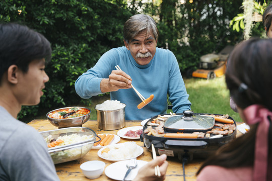亚裔老人喜欢和家人一起吃泰国烤肉。他用筷子夹着香肠。