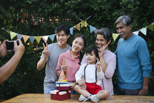 在户外的生日庆祝派对上，用智能手机拍摄亚洲家庭肖像。