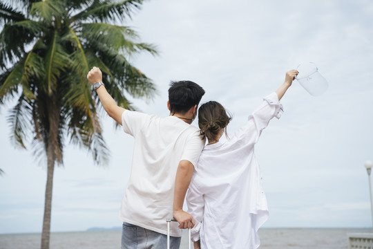后视图-亚洲情侣旅行者在海上举手。