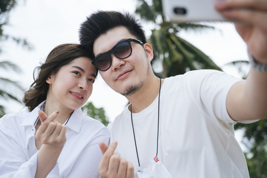 亚洲情侣旅行者在热带岛屿用智能手机自拍。