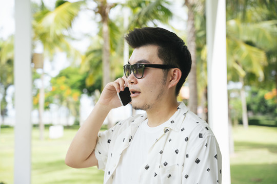 一位穿着休闲衬衫、戴着墨镜的亚洲商人在度假酒店打电话。