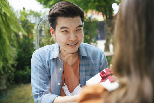 一个亚洲男人在户外院子里用礼盒给女友一个惊喜。他穿过障碍物送礼物。