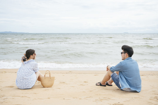 一对亚洲夫妇坐在海边的沙滩上，互相看着对方。