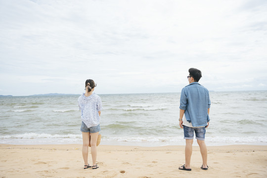 后视图-亚洲夫妇旅行者站在沙滩上看海的水平。