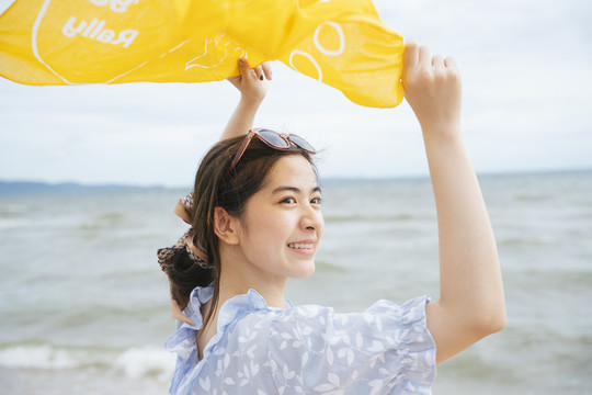 风和日丽的亚洲年轻女子在沙滩上玩黄围巾。