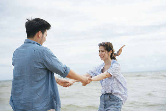 快乐浪漫的亚洲情侣旅行家牵手在沙滩上跳舞在夏天。