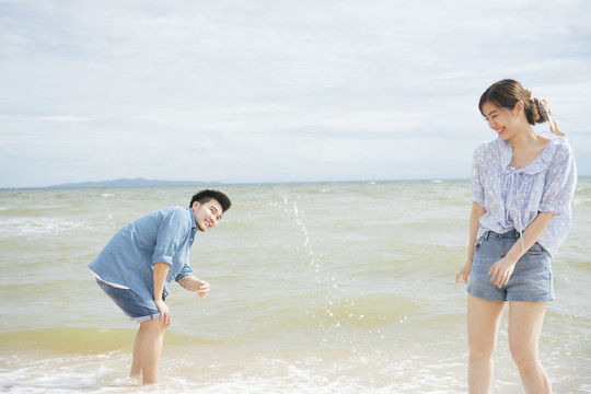 亚洲情侣旅行者在沙滩上玩泼水游戏。