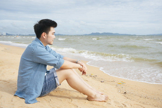 孤独的亚洲人在夏天独自坐在沙滩上看海。