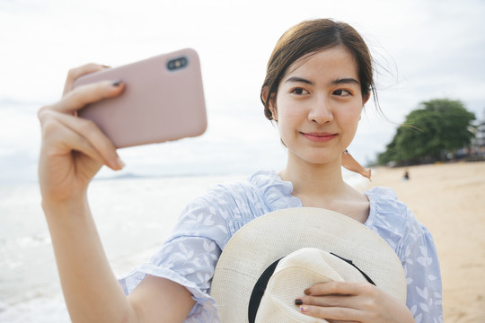 戴着帽子的亚洲情侣旅行者在沙滩上用智能手机自拍。