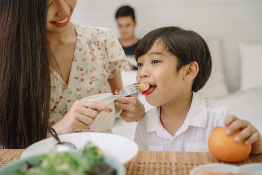 亚泰妈妈给儿子喂饭。一家人在家吃午饭。