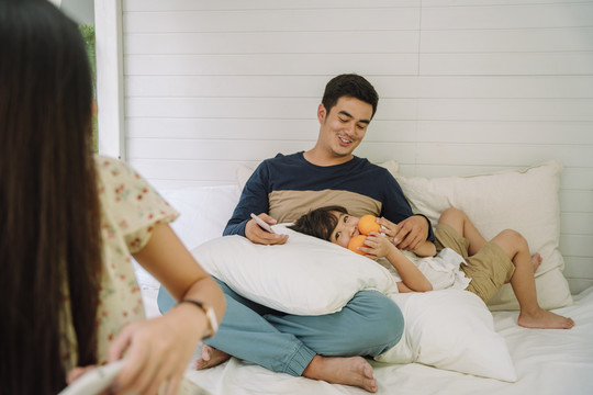 亚洲家庭在家里玩得很开心。父子俩在床上放松。儿子手里拿着桔子。