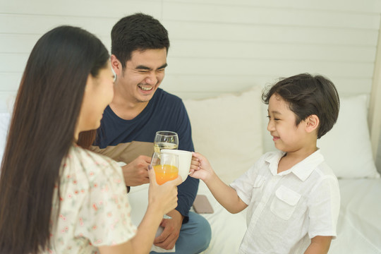 亚泰家庭用健康饮料欢呼和祝酒。牛奶和橙汁。一家人在家一起吃早餐。