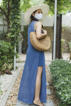 全长-美丽的亚泰旅游妇女穿着蓝色连衣裙，戴着面具和帽子，手拿篮子包在公园户外。