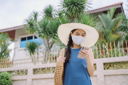 美丽的亚泰旅游妇女戴着口罩在旅行时使用智能手机。