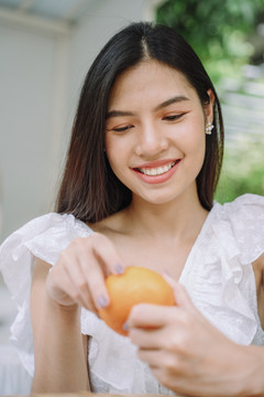 美丽的亚洲长黑发女人的特写肖像，穿着白衬衫，带着橙色水果。