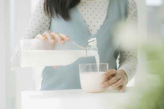 特写镜头-年轻美丽的亚洲孕妇从瓶子里倒鲜奶。