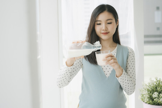 年轻漂亮的亚洲孕妇从瓶子里倒鲜奶。