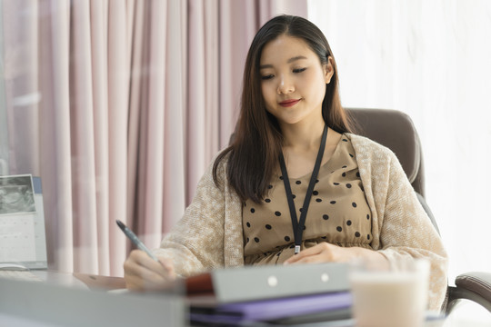 美丽怀孕的成年亚泰女商人在办公室工作。