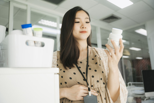 美丽的怀孕的亚洲女商人正在读医药瓶上的标签。