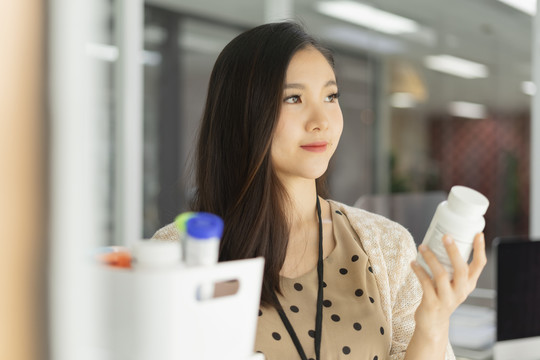 美丽的怀孕的亚洲女商人正在读医药瓶上的标签。