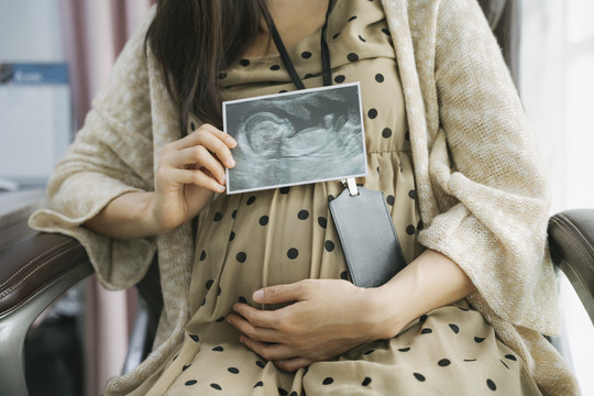 美丽怀孕的亚洲女商人抱着肚子和电影超声波扫描。