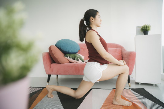 美丽怀孕的亚洲女商人在家里做伸展腿和膝盖的运动。瑜伽。