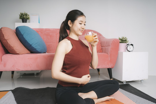 美丽的亚洲孕妇在家运动后喝橙汁。