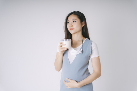 一位快乐美丽的亚洲孕妇，喝着一杯白色背景的新鲜隔离液。