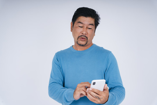 身着蓝色长袖衬衫的老人使用智能手机的画像，表情激动。