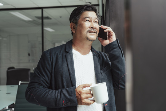 亚洲商人在会议室里拿着咖啡杯和智能手机。