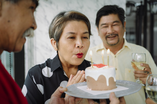 老人们用蛋糕庆祝生日聚会。老妇人在蛋糕上吹蜡烛。