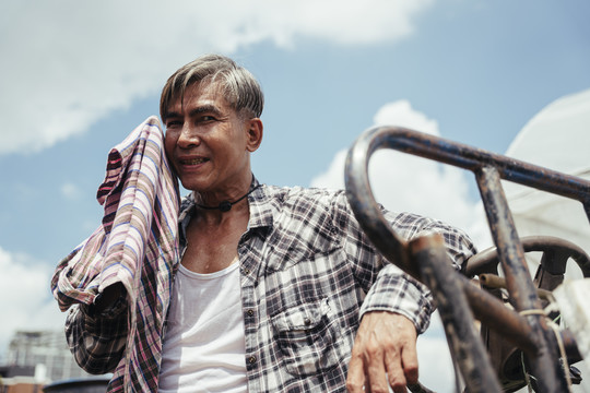在当地农场工作后在拖拉机上休息的亚洲老年农民。