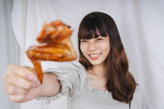 快乐的亚洲女人展示烤鸡翅的肖像。