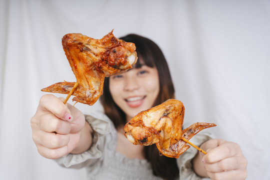 快乐的亚洲女人手持两只烤鸡翅的画像。
