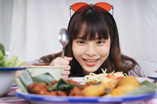 一个流口水的年轻亚洲女人拿着勺子看着桌上的食物。
