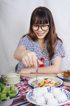 戴眼镜的亚洲年轻女子用叉子吃米粉的画像。