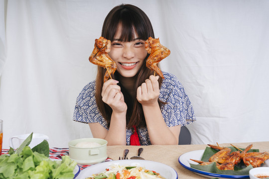 亚洲年轻女子手持烤鸡翅棒的画像。是一种食物概念。
