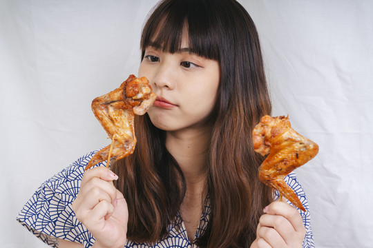 亚洲年轻女子手持烤鸡翅棒的画像。是一种食物概念。