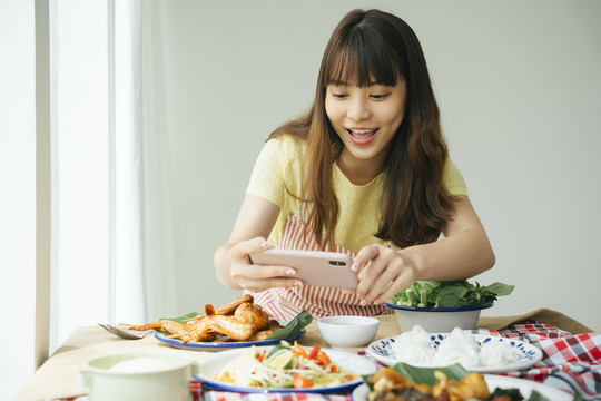 亚洲年轻女子在家里用智能手机为伊桑食品拍照的照片。