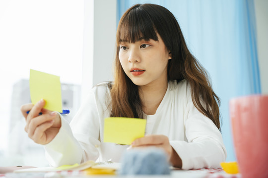 年轻的亚洲黑发女子在便笺纸上写作和计划。